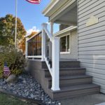 Front porch with gray composite steps, white railing, and black balusters beside a home entry.