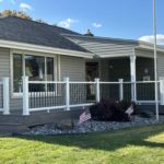 Long front porch with gray composite decking, white railing, and black balusters across a ranch-style home.