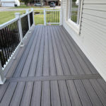 Gray composite porch deck with white railing and black balusters along the front of a home.