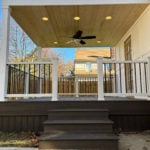 Covered backyard deck with dark composite boards, white railing, wood ceiling, recessed lights, and ceiling fan.