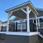 Elevated covered deck with white pavilion roof, black railing, and stairs attached to a gray house.