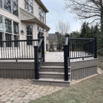 Gray composite deck with black railing, center stairs, and curved edge beside a two-story home.