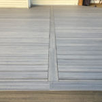 Gray composite deck surface with picture-frame border and center divider detail near a house exterior.
