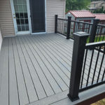 Small gray composite deck with black metal railing outside a back door on an elevated home.