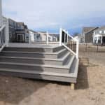 Gray composite deck with tiered stairs, white railing, and black balusters in a new construction backyard.