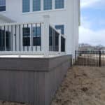 Gray elevated deck with white railing and black balusters attached to a two-story white house.
