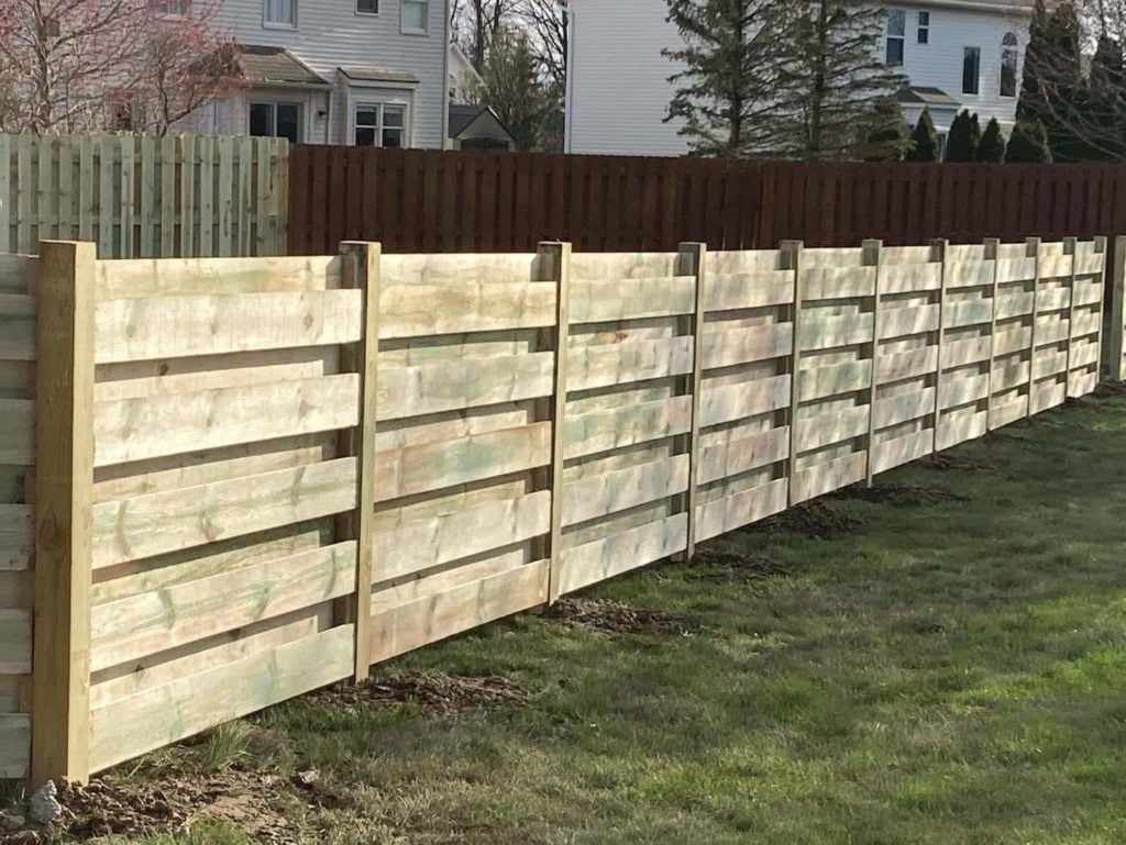 Modern horizontal wooden shadow box fence with staggered slats in a residential backyard.