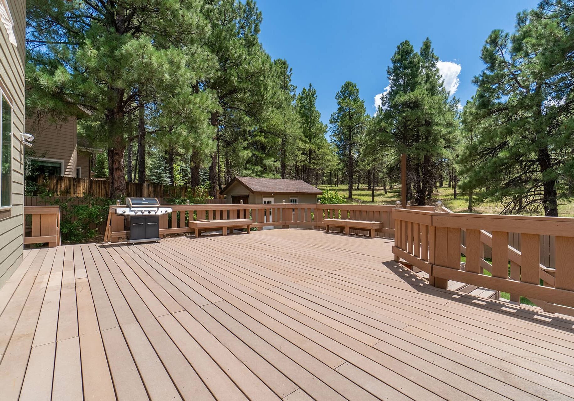 Spacious backyard composite deck with built-in bench seating, railing, and grill by Patriot Outdoor Structures.