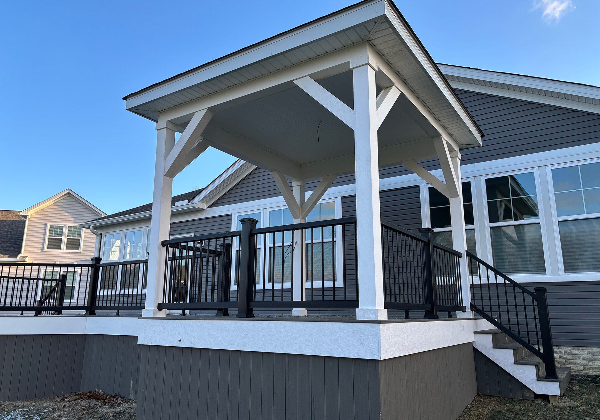 Elevated covered deck with white pavilion roof, black railing, and stairs attached to a gray house.