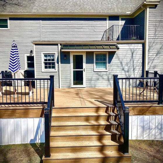 An elevated wood deck with black aluminum railings and two sets of stairs featuring white vertical board skirting around the base.